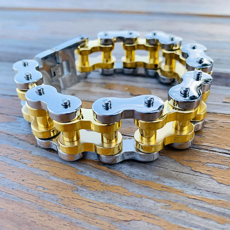 A bracelet made of silver and gold-colored motorcycle chain links laid out on a wooden surface.