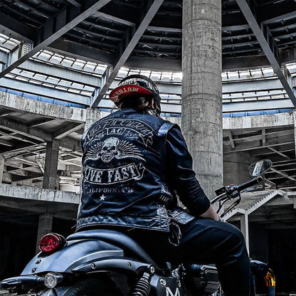 Person sitting on a motorcycle wearing a leather jacket with a skull design in an industrial setting.