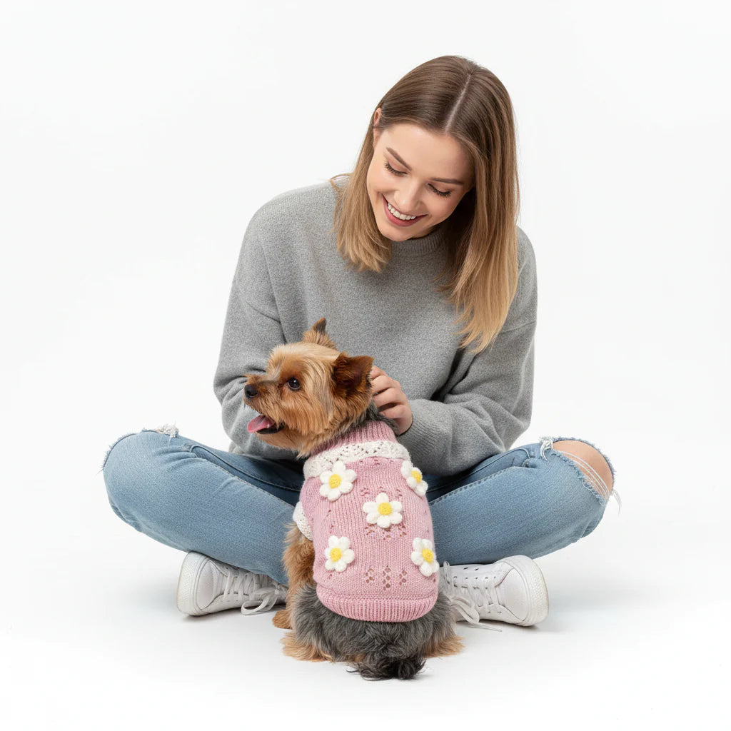 Woman sitting with a small dog wearing a pink sweater with white flowers on a white background